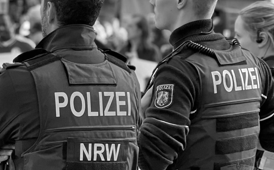Zwei Polizeibeamte in Schutzwesten von hinten, Schwarz-Weiß-Aufnahme